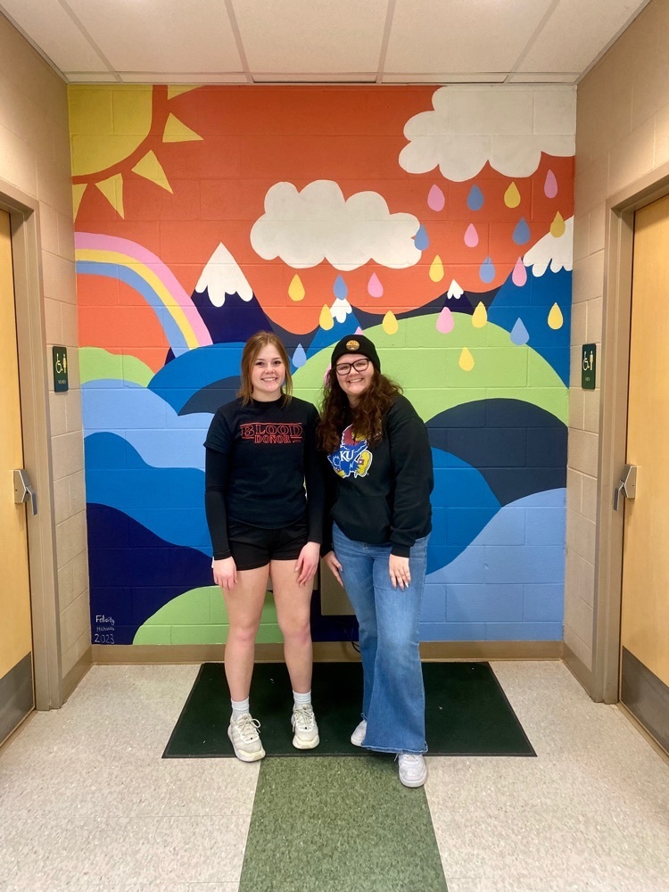 two girls smile in front of a mural